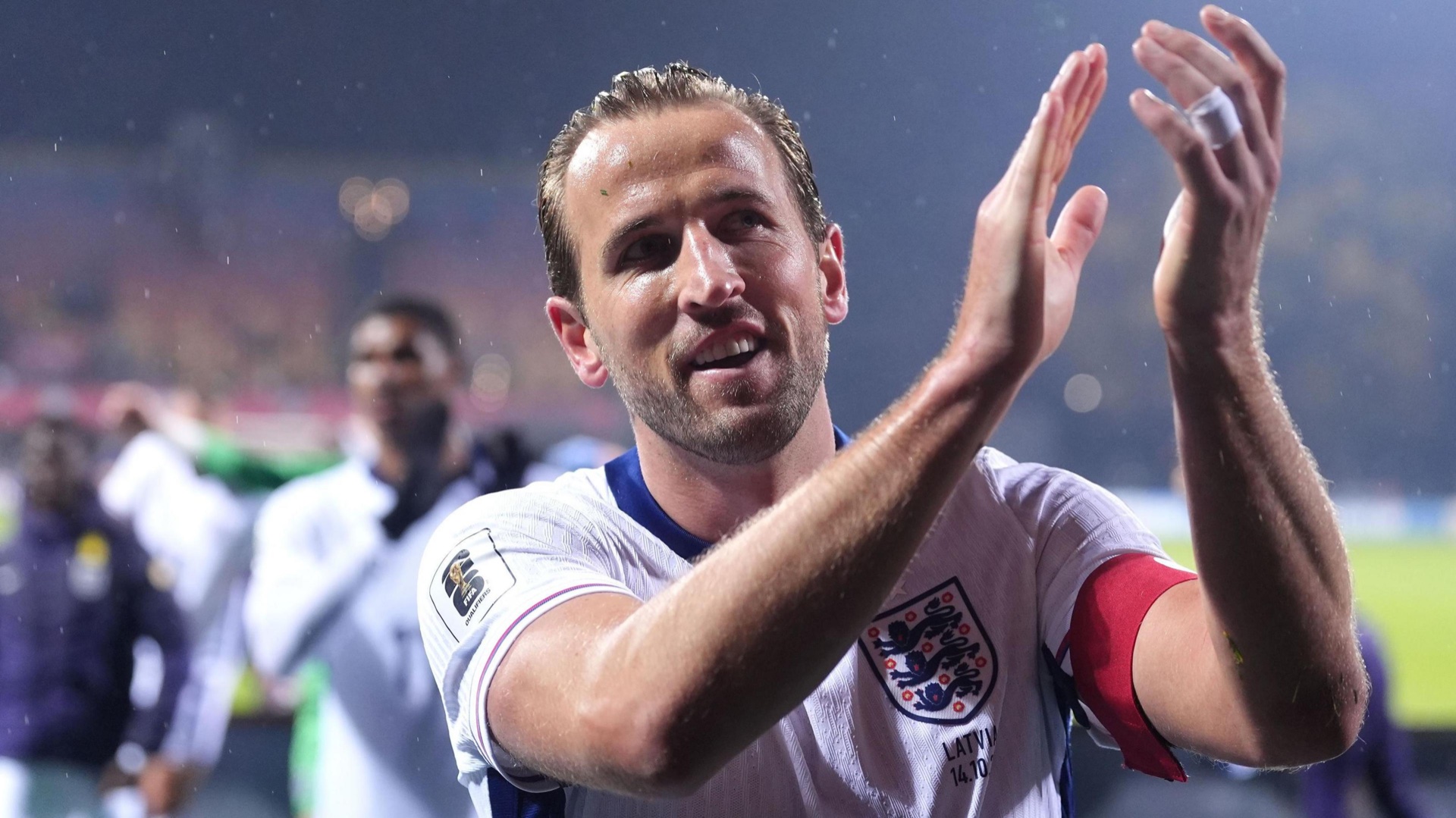 Harry Kane wearing England’s white kit and captain’s armband as he applauds supporters after a match.