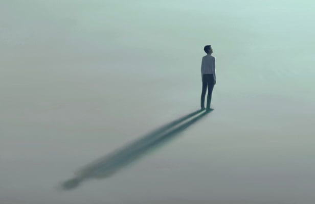 A solitary person standing in a pale open space while casting a long shadow