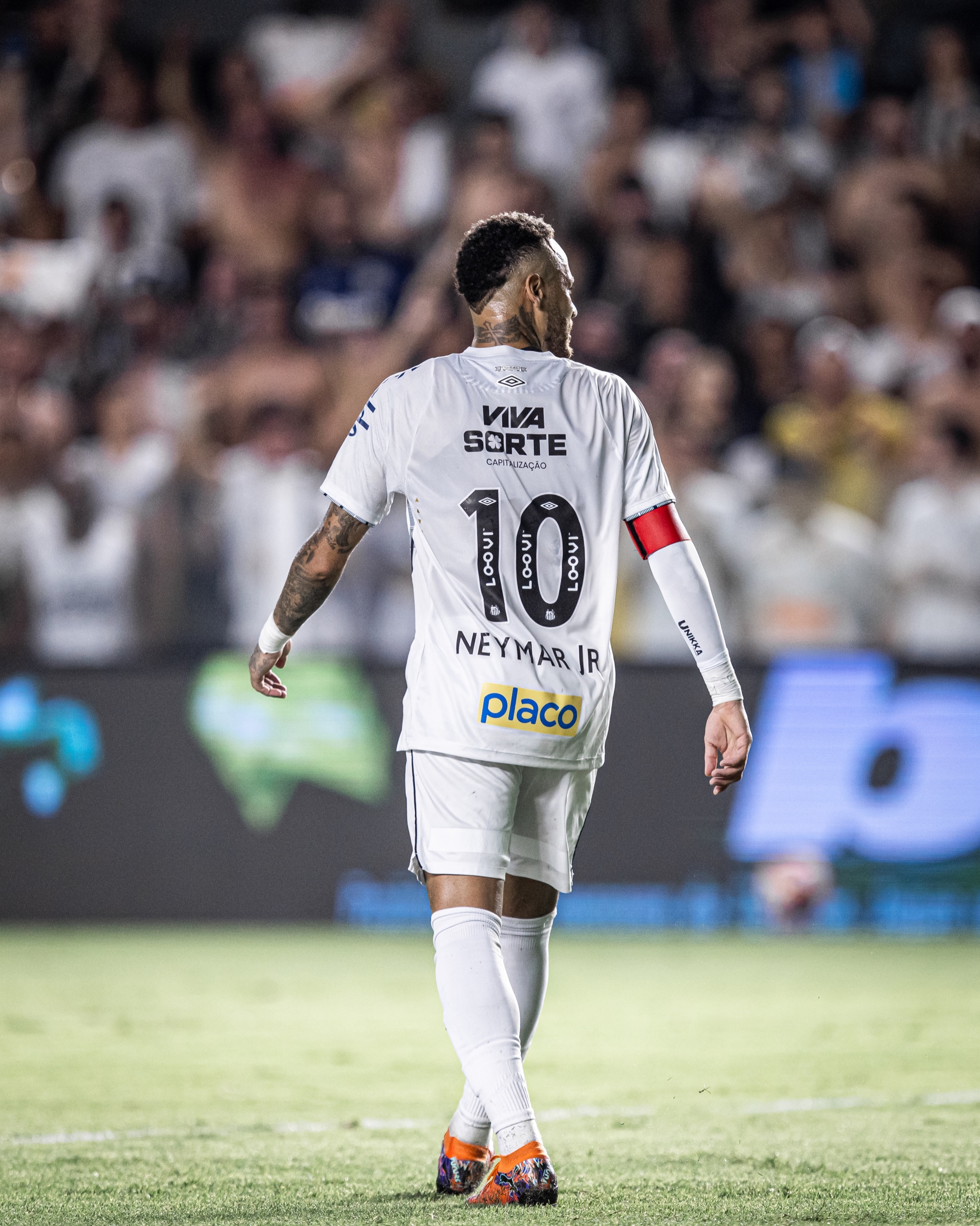 Neymar Jr. walking on the pitch in a white Santos number 10 shirt and captain's armband.