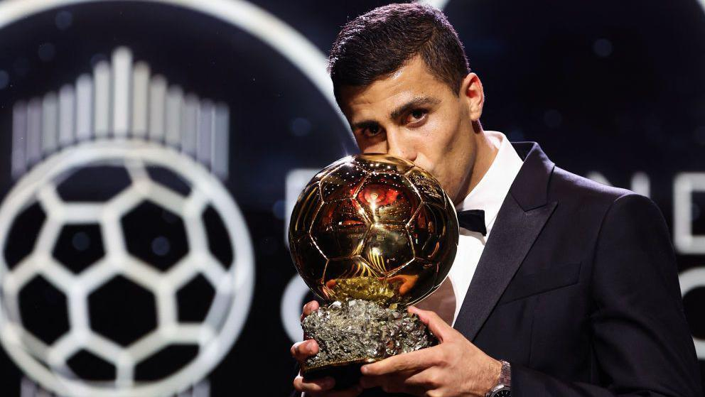 Rodri kissing the 2024 Ballon d’Or trophy while wearing a black tuxedo at the awards ceremony.