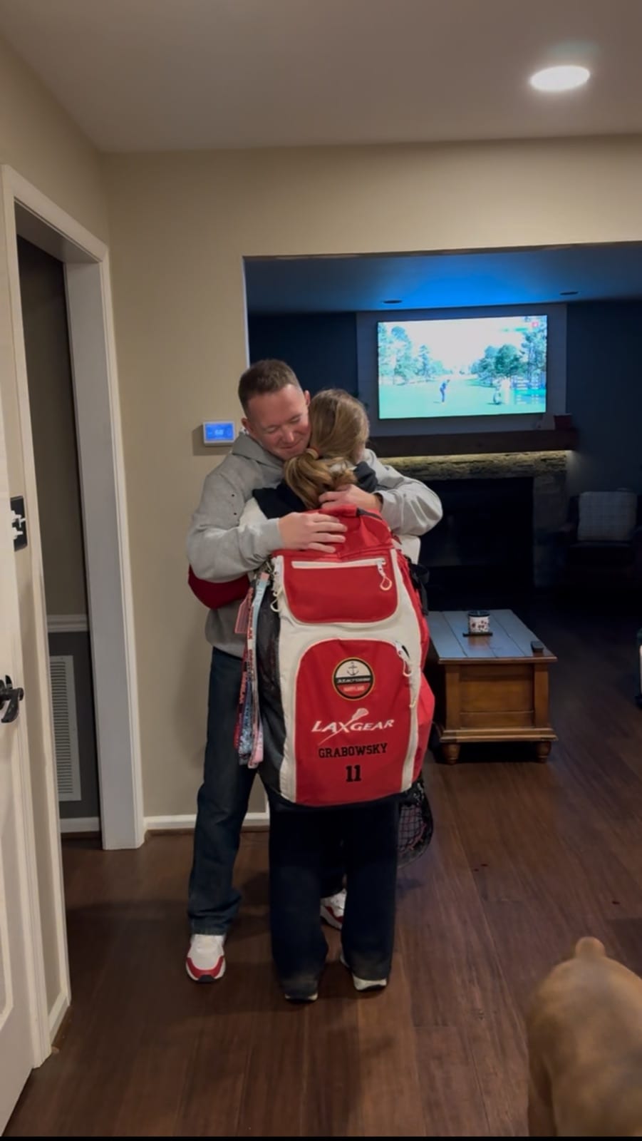 Sadie hugging her dad in a home while wearing a lacrosse backpack