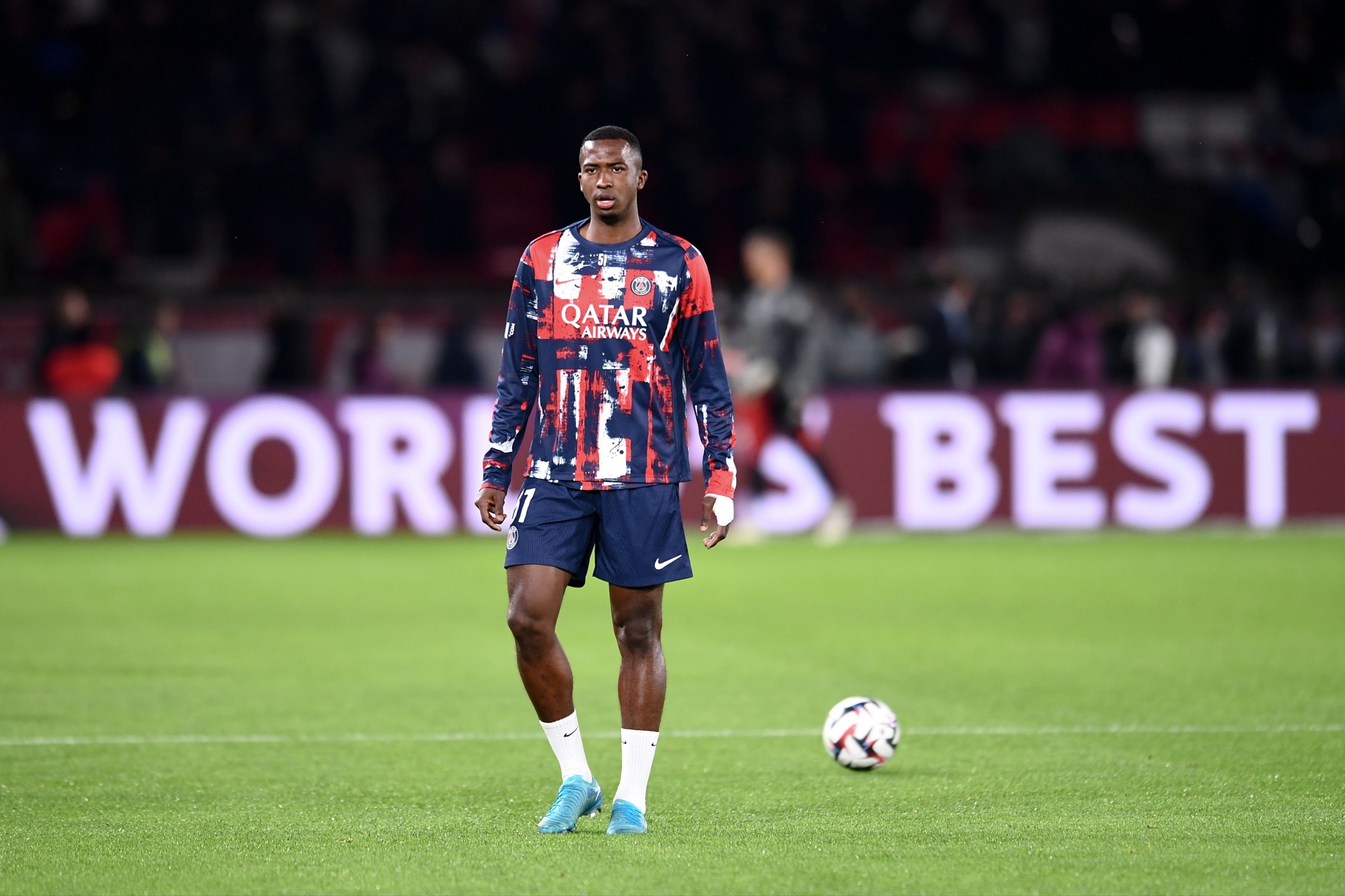 Willian Pacho standing on the pitch in a Paris Saint-Germain warm-up kit before a Ligue 1 match.