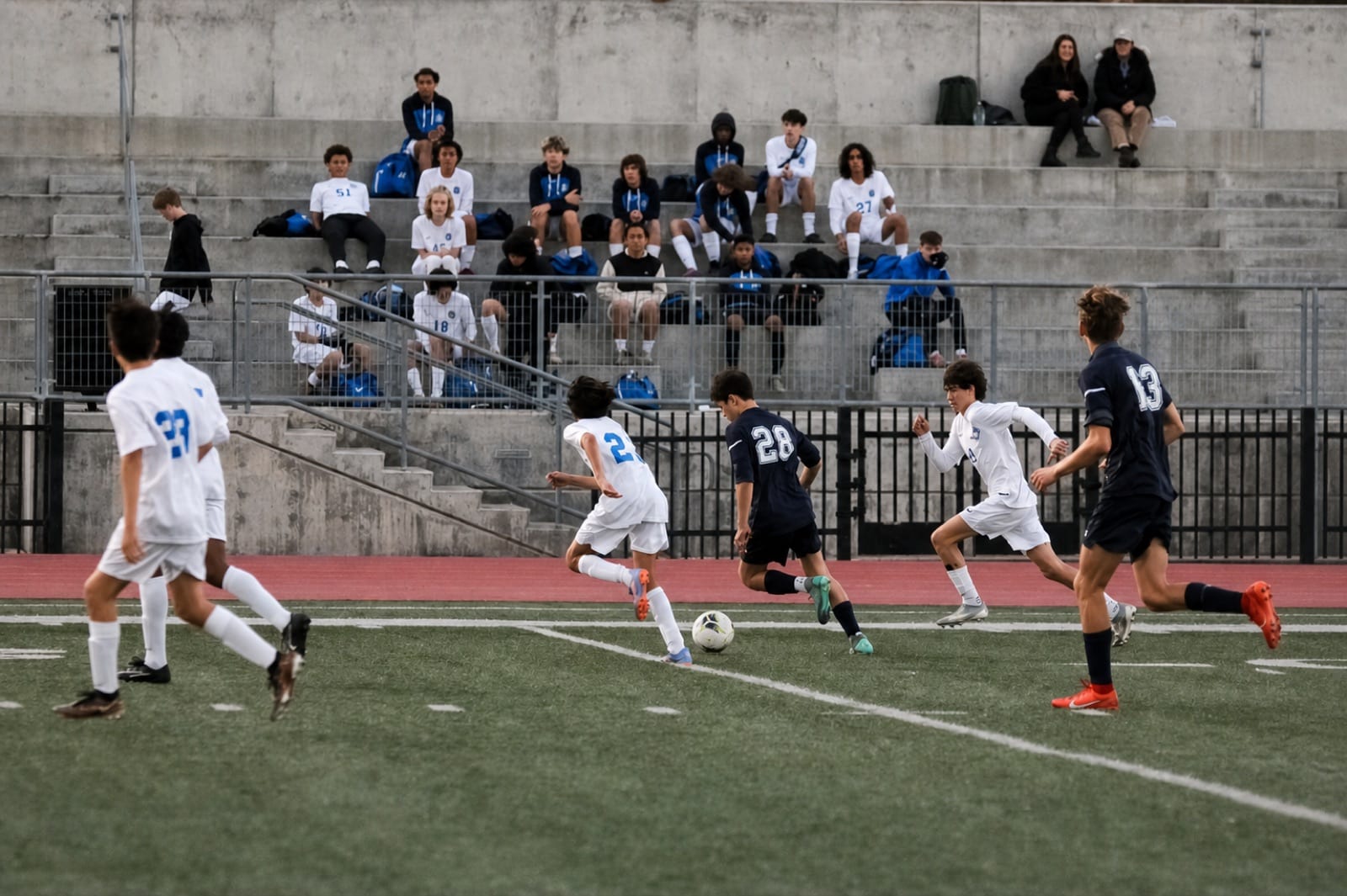 Soccer players competing for the ball during a game in front of concrete bleachers